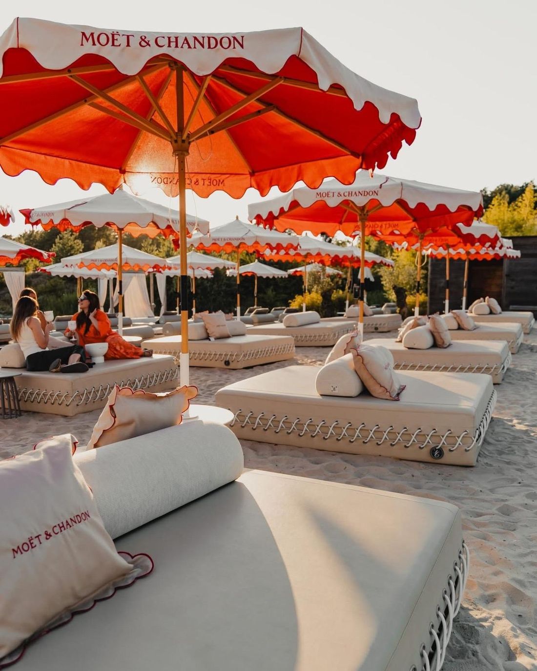Rijen Le Couchon pouffes met kussens en rolkussens op het zand bij zonsondergang